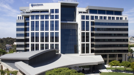 Qualcomm building features a modern design with large glass windows and a curved roof in a landscaped setting.