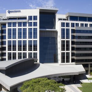Qualcomm headquarters, a modern glass building with multiple stories and a distinctive curved roof, surrounded by green landscaping.