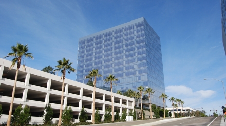 Modern office building with a glass facade, surrounded by palm trees and a parking structure in La Jolla, California.