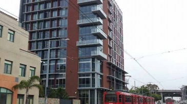 Modern building at 15th and Commercial, with a red trolley approaching along the tracks.