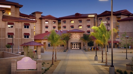 Bachelor enlisted quarters building featuring palm trees, modern architecture, and landscaped pathways at dusk.