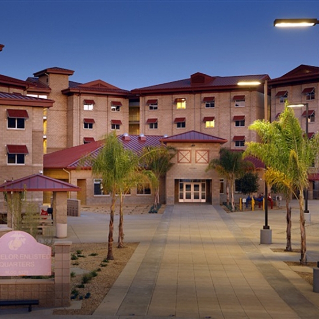 Bachelor enlisted quarters building featuring palm trees, modern architecture, and landscaped pathways at dusk.