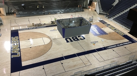 Basketball court view inside California Baptist University Event Center during setup, featuring seating and construction equipment.