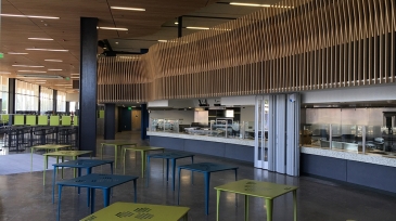 Modern cafe interior at SDCCD Bookstore featuring green and blue tables and a light wood ceiling design.
