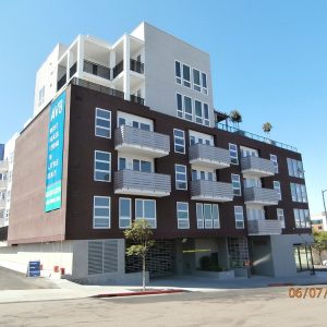 Modern apartment building AV8 in Little Italy featuring balconies and a prominent banner. Blue sky overhead.