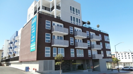 Modern apartment building AV8 in Little Italy featuring balconies and a prominent banner. Blue sky overhead.