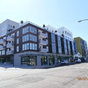 Modern apartment building exterior with multiple balconies and large windows, surrounded by streets and parked cars.