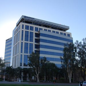Qualcomm building with modern design, glass facade, and surrounding palm trees, set against a clear blue sky.