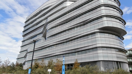 Modern UCSD building featuring sleek glass design and unique architectural elements against a partly cloudy sky.