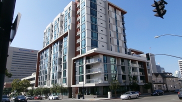 Modern multi-story building featuring glass facades, located in an urban environment with nearby traffic and pedestrians.